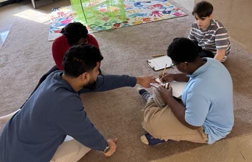  Teacher and students sitting on the floor doing class work